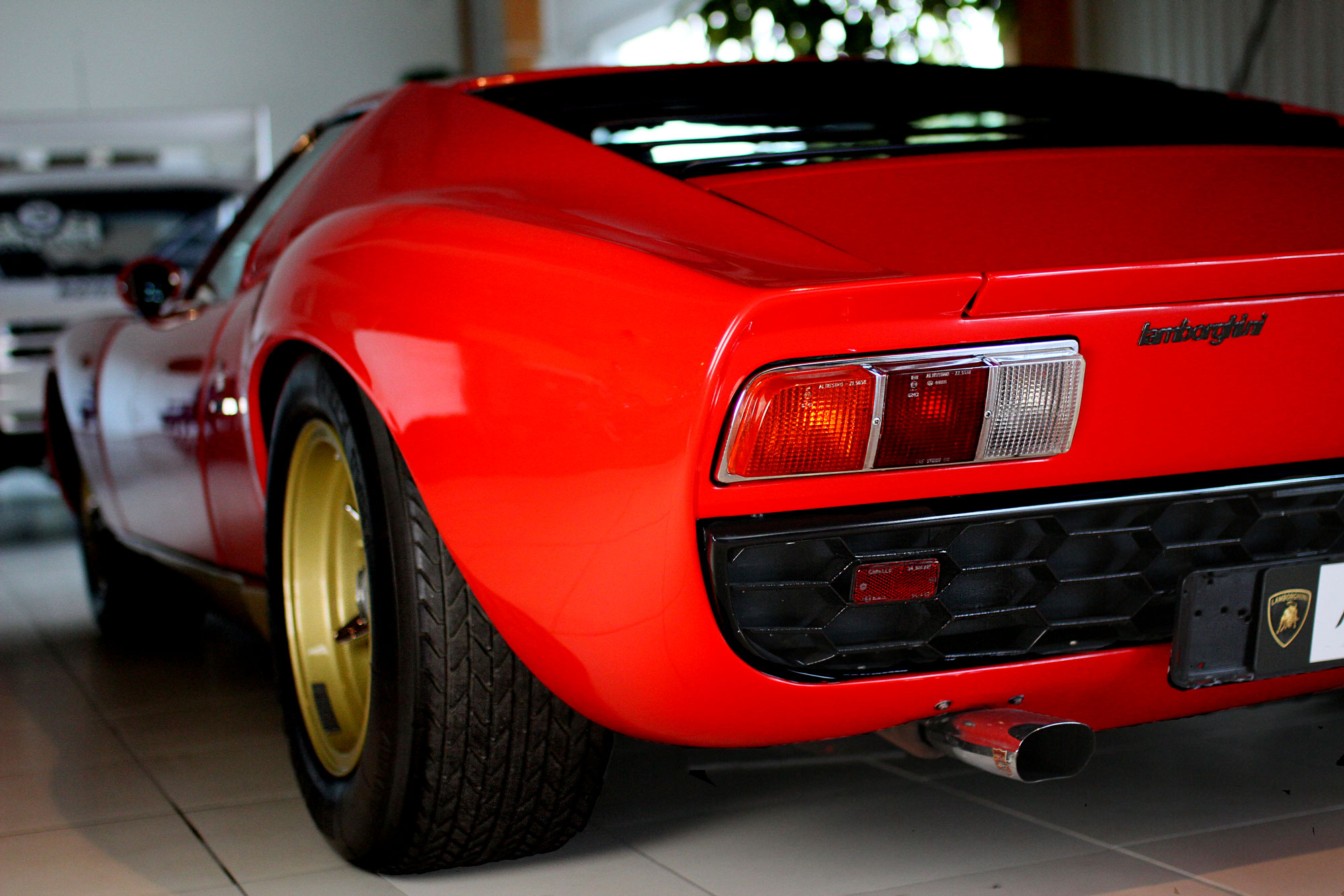 Lamborghini Miura Red with golden rims and Lambo brand on the back with a Metro 6R4 in the background 