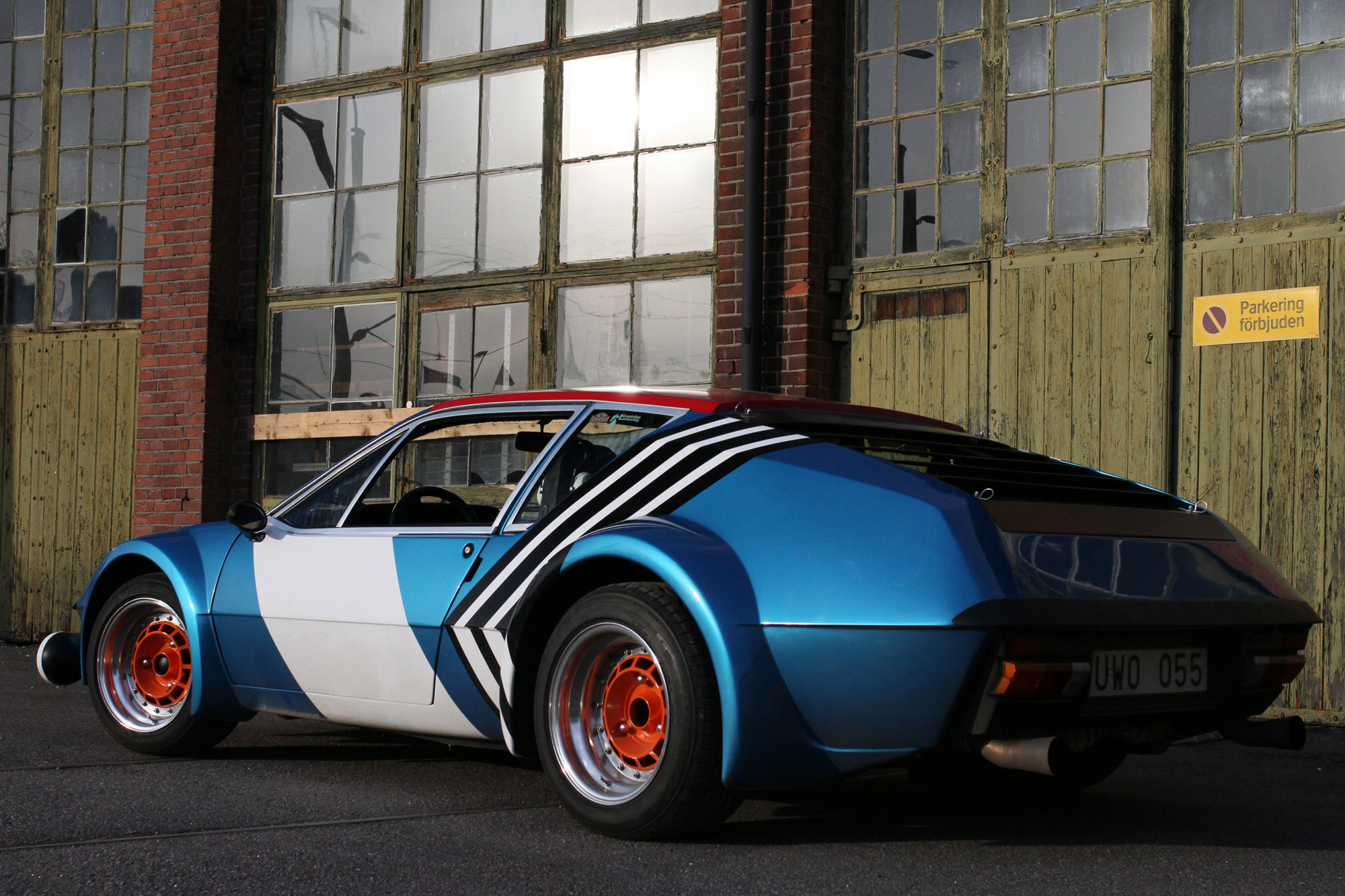 The sun is shining on the Renault Alpine A310 infront of a Parking Forbidden sign.
